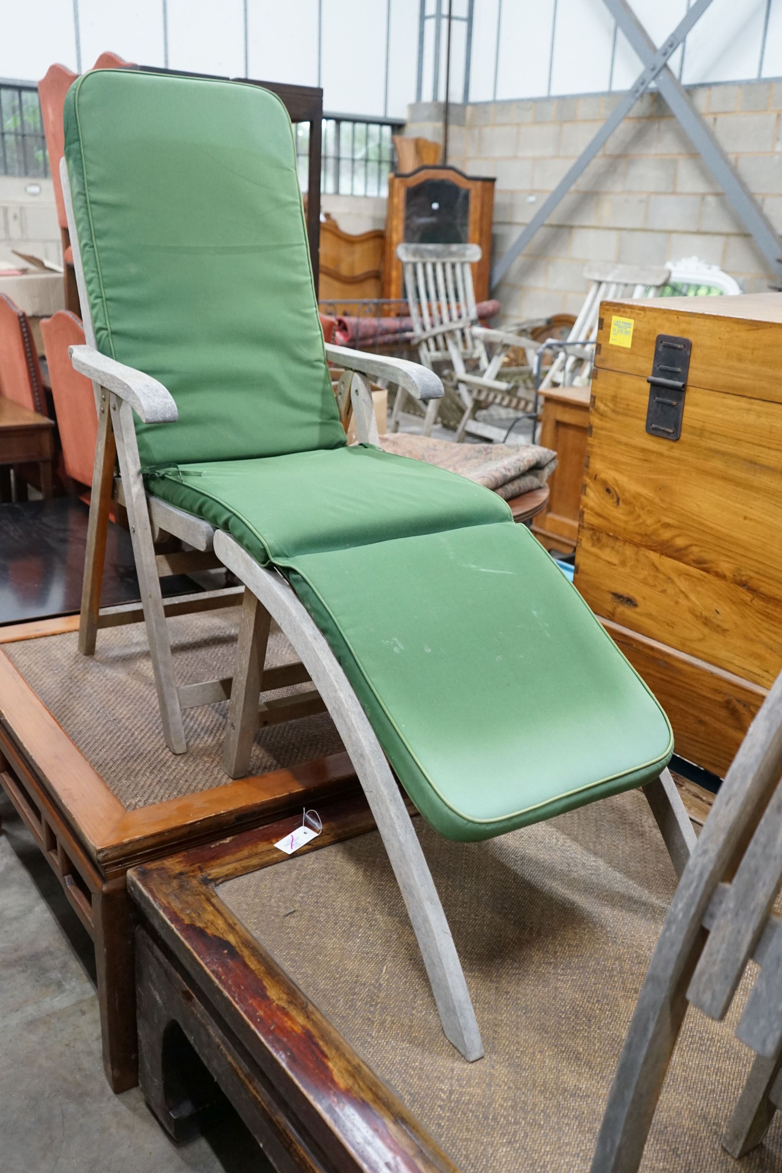 A pair of weathered teak folding reclining garden elbow chairs with footrests and seat pads